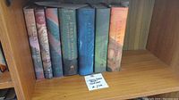 Photo of six Harry Potter hardcover books aligned on a wooden shelf, showing spines with titles and author name.