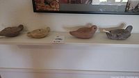 Four vintage artisan clay oil lamps displayed on a white shelf, shaped mainly as birds, with one lamp showing floral engravings, varying in earth tones.