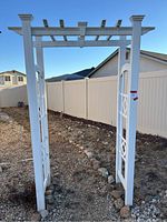 Full front view of white wooden pergola standing on ground with decorative side panels and lattice top under clear sky