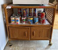 Front view of the rattan cart showing canned goods on open middle shelf and closed cabinets below.