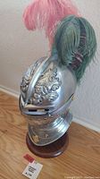 Front and side view of metal replica knight helmet showing detailed embossed ornamentation and base stand