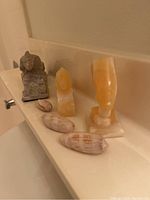 Photo showing three stone figurines (gray sphinx, yellow-orange monkey face, and tall yellow head), and three decorative sea shells arranged on a bathroom ledge.