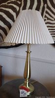 Full view of the lamp including white pleated lampshade and brass base on a table.
