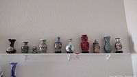 Wide photo showing all nine souvenir vases and the white wall shelf they sit upon.