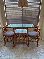 Full view of vintage bamboo and rattan dinette set with rectangular glass top table and two chairs with fabric cushions.