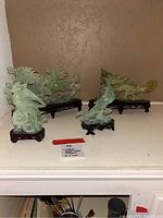 Four vintage Chinese jade figurines displayed on wooden stands showing phoenix birds and mythical creatures.