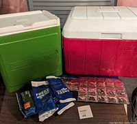 Two Coleman coolers, one green Party Stacker and one larger red cooler, with assorted cooler ice packs laid out in front.