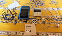 Two iPods, charging cable and earbuds laid out on a patterned tablecloth showing their condition and accessories.