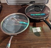 Two 12-inch frying pans side by side with lids on, showing exterior sides and handles.