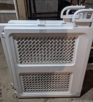 Side view showing one white house gate with large perforated panel and smaller lower section for visibility and airflow.