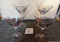 Four hand-painted martini glasses arranged in two pairs, placed on a dark woven fabric with a white background, displaying their different sizes and designs.