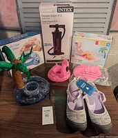 Photo showing palm tree and flamingo inflatable drink floaties, Intex air pump, water shoes size 8, and additional small pink inflatable item on a wooden surface.