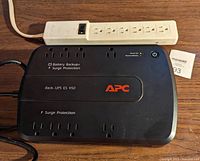 Black APC Back-UPS ES 450 battery backup and surge protector unit with power bar on wooden surface.