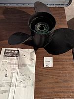 Photo of black three-blade boat propeller with instruction manual on wooden surface