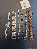 Photo showing 6 costume jewelry bracelets laid flat, various designs and colors including rhinestones and beads, one has a loose ball charm.