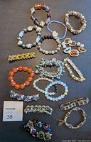 Top down view of 17 assorted costume bracelets varying in bead styles, colors, and metal accents on dark background