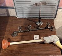 Photo of three items on wooden surface: bird-headed plunger, towel holder made from tap closers, and metal hand towel rack