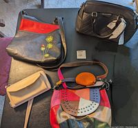Five handbags arranged on a flat surface showing variety in size, style, and color