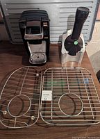 Keurig coffee maker, Yonanas frozen dessert maker, and two metal sink protectors displayed together on table