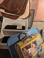 Photo showing white plastic dog stairs with black carpeted steps and stack of brown and cream colored dog blankets or mats. Also visible is a blue plastic container with an unopened packaged car seat hammock on top.