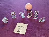 All 6 Swarovski crystal animal figurines displayed on purple fabric with golf ball for size reference.