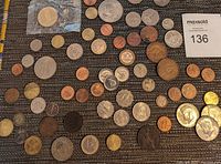 Top-down photo of approximately 55 mixed world coins and tokens including Canadian, US, Cuba, France, and UK coins on a dark fabric surface.