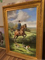 Full view of large framed equestrian oil painting with rider and dogs in a countryside setting.