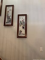 Two vertical wood-framed artworks hung on a light gray wall