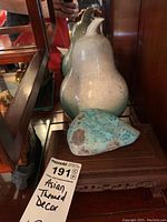 Pear figurine and turquoise rock on wooden stand inside glass display case.