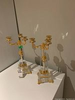 Pair of acrylic and gold tone candle holders on white surface, showing front and side views, with green labels and MaxSold tags visible.