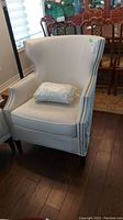 Front view of white upholstered armchair with silver nailhead trim and patterned pillow on seat.