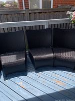 Five dark brown plastic outdoor chairs arranged on a blue wooden deck, showing the woven rattan-style texture and curved backrests.