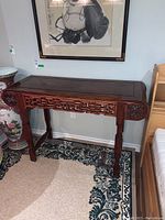 Front view of wood console table showing intricate carved apron and legs, dark wood finish.