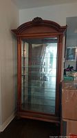 Full view of the tall wooden display cabinet with glass door and shelves.