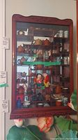 Front view of wooden display cabinet showing glass door, wood shelves, and mirrored back with various decorative items inside (not included).