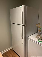 White GE refrigerator freezer with top freezer and bottom fridge shown from an angle in a basement room with wooden floor.