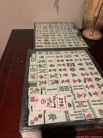 Photo of two boxes of Mahjong tiles showing various traditional Chinese characters and symbols in red, green, and black ink on white tiles.