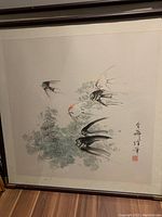 Framed print showing several fish swimming among aquatic plants with calligraphy and a red seal in lower right corner, behind glass.