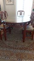 Full view of wooden dining table with glass overlay and six matching chairs on a patterned rug.