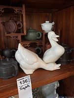 Wooden display stand with assorted teapots and two white ceramic ducks on shelf