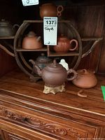 Full view of five clay teapots arranged on circular wood stand with Buddha figurine on bottom shelf