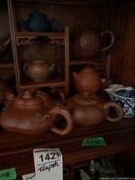 Multiple clay and porcelain teapots arranged on carved wood shelf