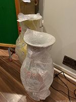Photo of two bubble-wrapped large decorative vases side by side on floor.