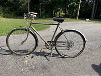Side profile of the antique full-sized adult bicycle showing entire frame, handlebar, seats, and wheels outdoors on paved surface.