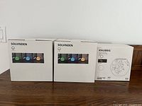 Three packages of Ikea lights displayed together on a wooden surface, two SOLVINDEN sets and one KNUBBIG set.
