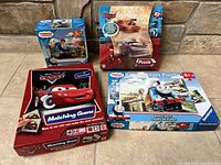 Four mixed kids toys and puzzles: two Thomas & Friends Ravensburger puzzles, one Cars puzzle, and one Cars matching game.