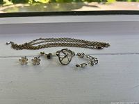 Photo showing small collection of jewellery pieces laid out on a white surface including daisy earrings without backings, Pilgrim branded ring, chain necklace, and two pairs of clip-on earrings.