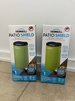 Two boxed Thermacell Patio Shield mosquito protection units standing on a tiled floor against a white wall.
