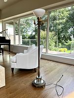 Full view of the vintage brass torchiere floor lamp showing the height, base, and plugged in electrical cord.