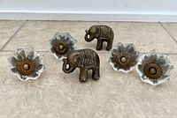 Top down view of 4 glass flower-shaped knobs with brass centers and 2 brass elephant handles showing details and condition.
